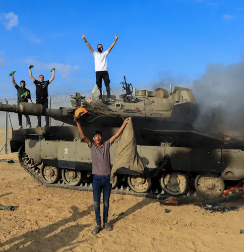 גברים חוגגים על טנק צבאי בוער ולצידו, ליד גדר הגבול, ועשן מיתמר ממנו