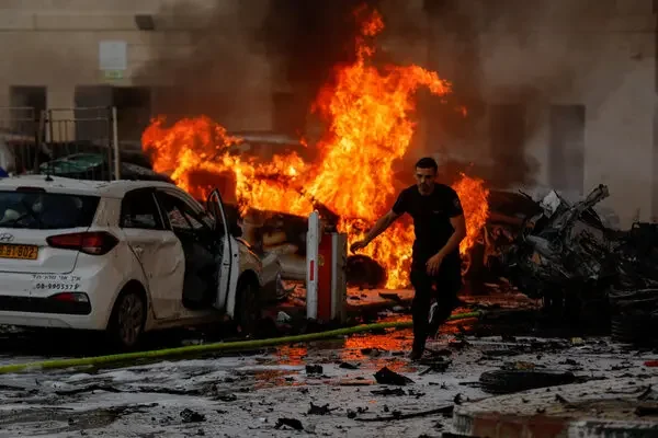 A man runs through a debris-strewn street past burning cars and tall flames